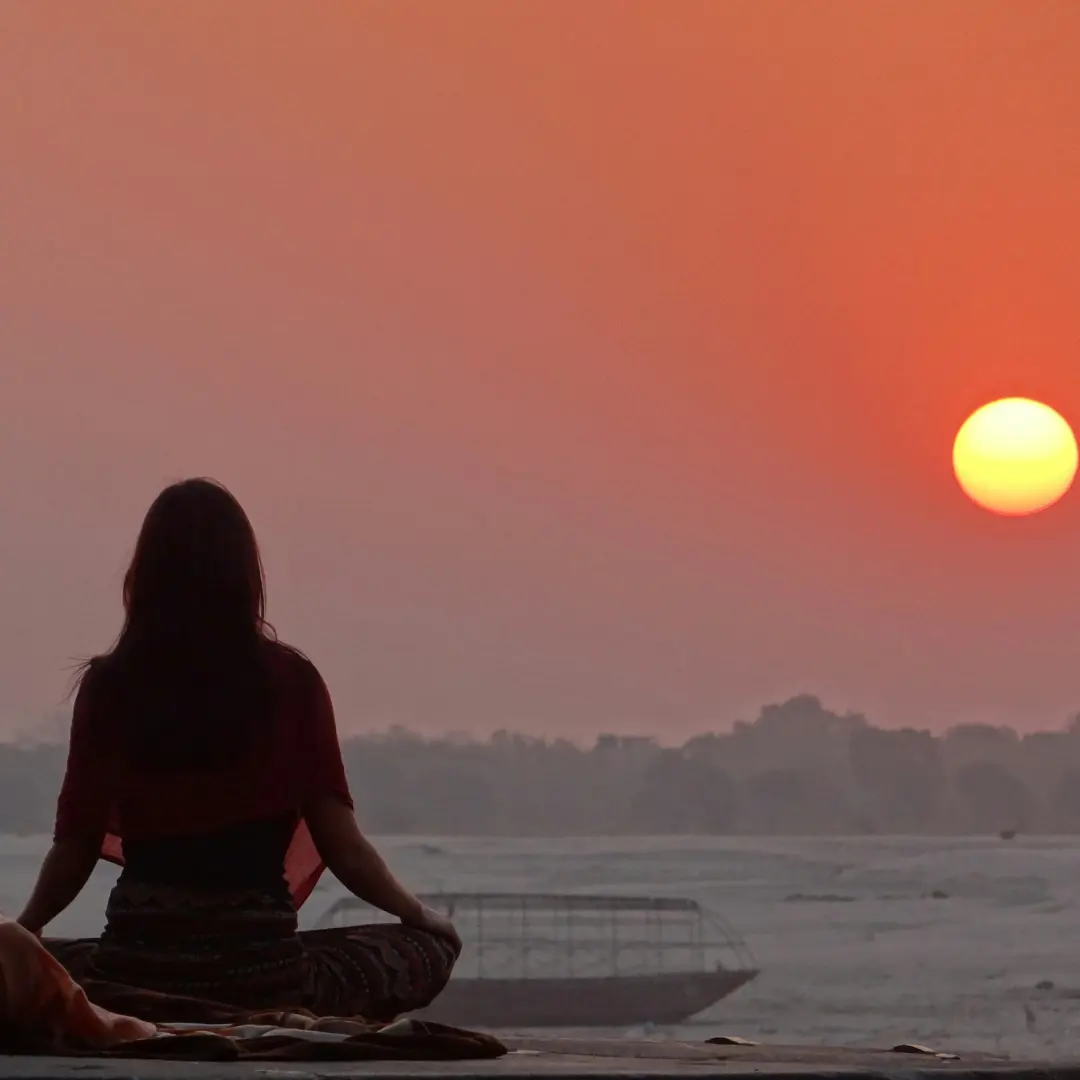 A figure seated in meditation by the water at sunset